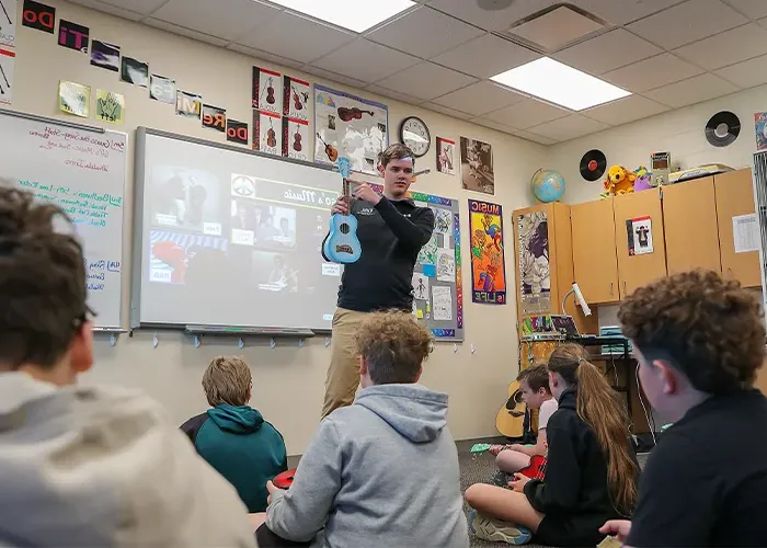 a 体育菠菜大平台 Music student holds up an instrument in front of a class of children